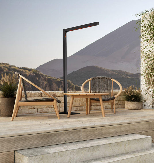 heatsail_heizstrahler_thetwig_minimalistisches_design_beheizt_eine_sitzgruppe_auf_einer_terrasse_aus_stein_und_holz_im_hintergrund_ist_eine_karge_vulkanische_landschaft_zu_sehen